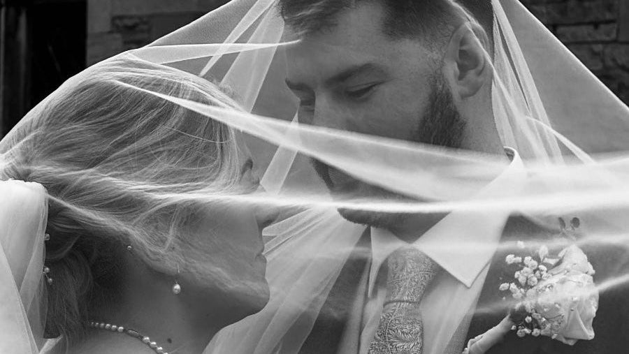 Black and white photo of a bride and groom under a veil